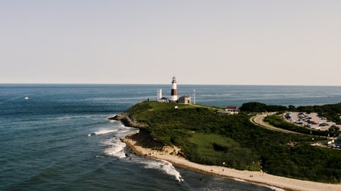 Stunning Aerial (Drone) Shot of Montauk Lighthouse in Long Island, New York surrounded by the blue sky, beach, seashore and the American flag