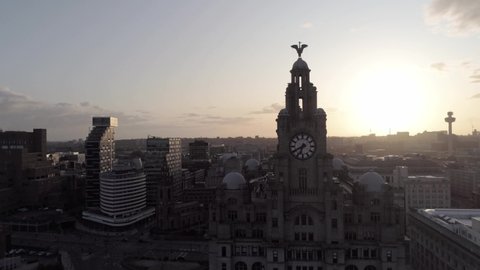 liverpool / United Kingdom (UK) - 08 18 2019: Liverpool city iconic Liver building skyline during glowing sunrise. Aerial orbit sunrise passing behind towers.