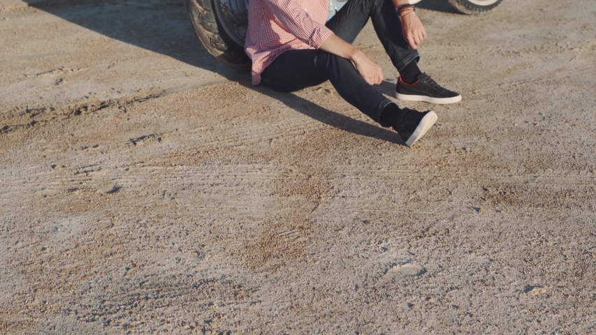 Young stylish motorcyclist sitting on his motorbike in the desert road during sunset 
