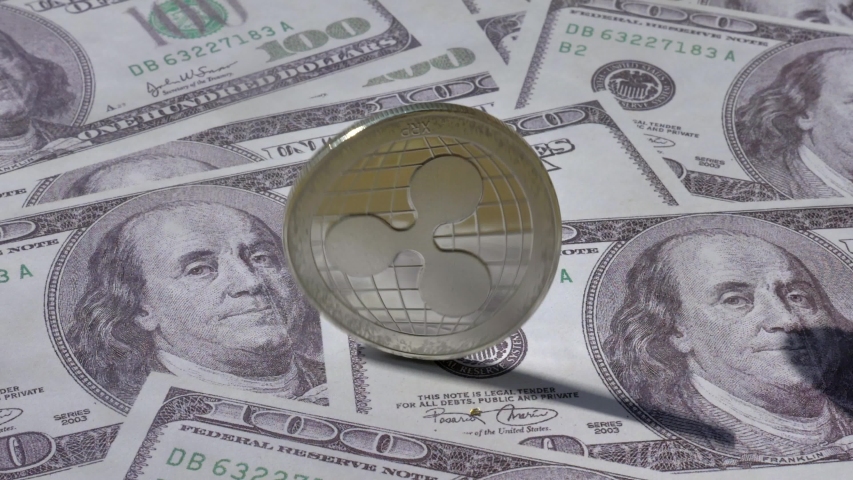 Silver Ripple Crypto currency coin spinning on One Hundred Dollar bills background and stopping  on its head side.