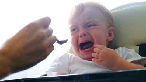 Close shot of mother feeding her little baby girl with teaspoon. She don't like to eat puree, cry and scream loudly. Child refuses to eat with tears