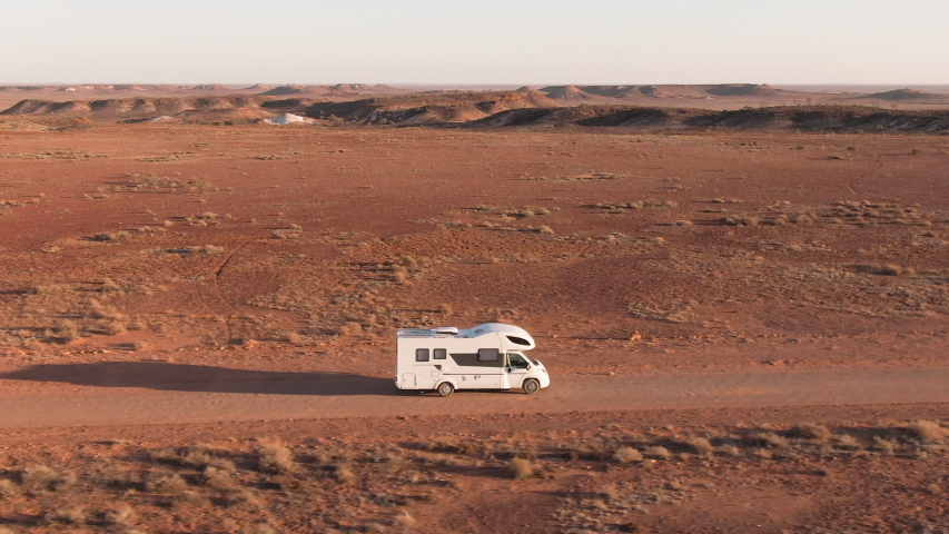 Aerial: Inspiring footage of caravan driving alongside the Breakaways, tourism scenic spot outside of Coober Pedy in the South Australian Outback.