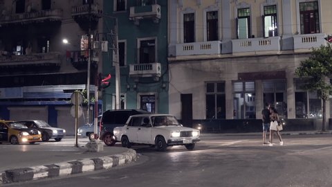 Havana / Cuba - 06 15 2019: A long shot of a prostitute getting into a stopped car at night at an intersection, in Havana, Cuba. The street is lit by street lights, several cars are waiting in line be