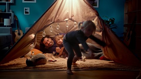 Mom, dad and two daughters play a monster in the evening in a toy tent
