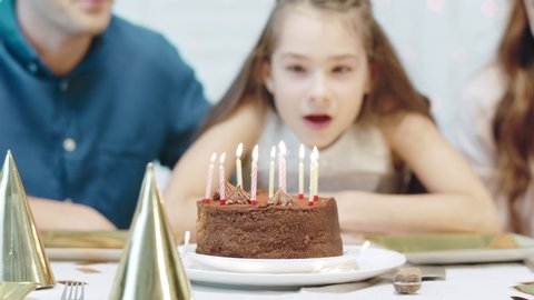 Closeup smiling girl blowing birthday candles in luxury house. Joyful family celebrating birthday party. Happy people clapping hands in living room.