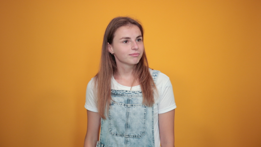 Young woman wearing white t-shirt, over orange background shows emotions