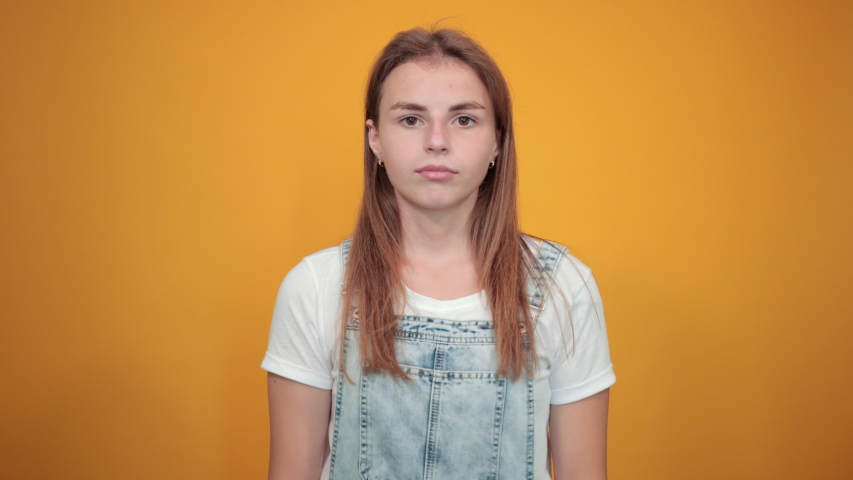 Young woman wearing white t-shirt, over orange background shows emotions