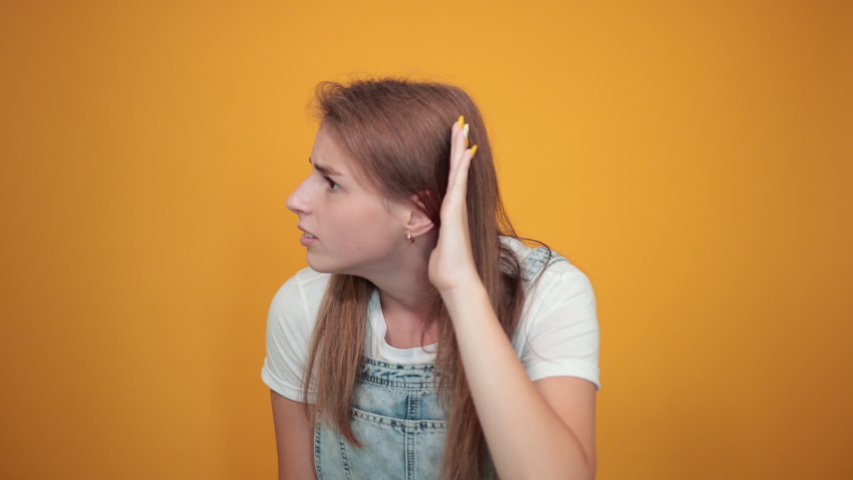 Young woman wearing white t-shirt, over orange background shows emotions