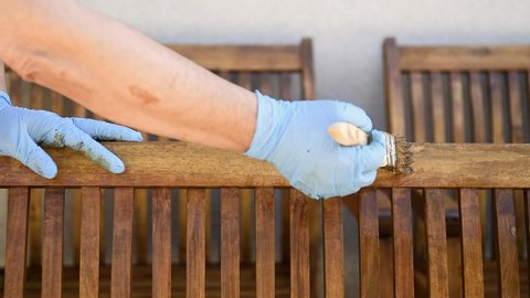 Adult carpenter craftsman painting with water-based paint the strips of a chair wooden garden. Housework, do it yourself. Footage.