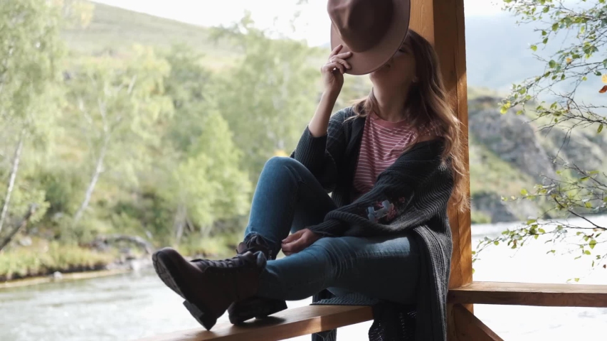 Attractive brunette covers her face with a hat enjoys nature in the mountains