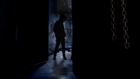 Hooded Man Behind Opening Door 4K Loop features a dark room with hanging chains swinging and a door opening to reveal a man in a black hooded and then closing again in a loop