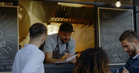 Cheerful waiter taking order from multi-racial customers at counter, Mexican street food served from a food truck. 4K UHD RAW graded footage