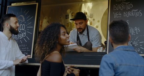 Cheerful waiter taking order from multi-racial customers at counter, Mexican street food served from a food truck. 4K UHD RAW graded footage