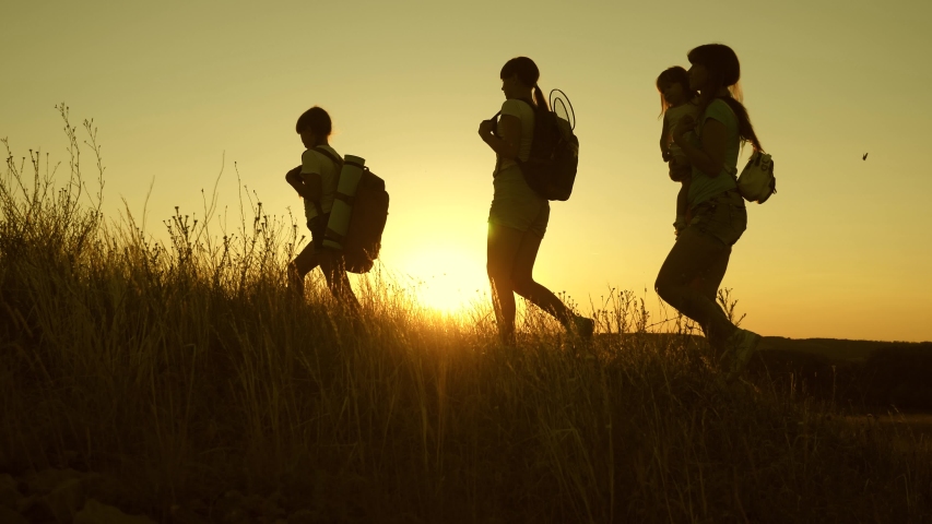 Children and mom with backpacks travel down the mountains in rays of the sun. Mom and daughters go camping. joint work of tourists. Slow motion. butterfly flies in the sunset light. teamwork travelers | Shutterstock HD Video #1036708421