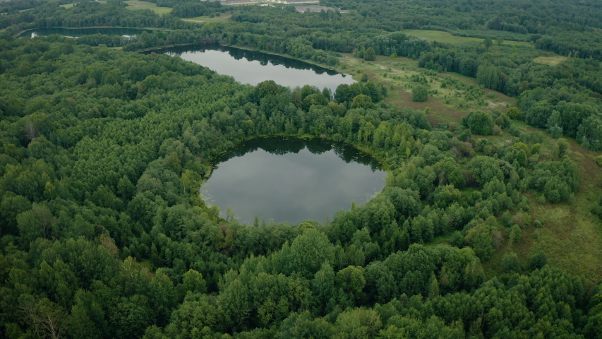 Aerial view of lakes with growing forest, reflection of sky and clouds in the water, nature landscape.