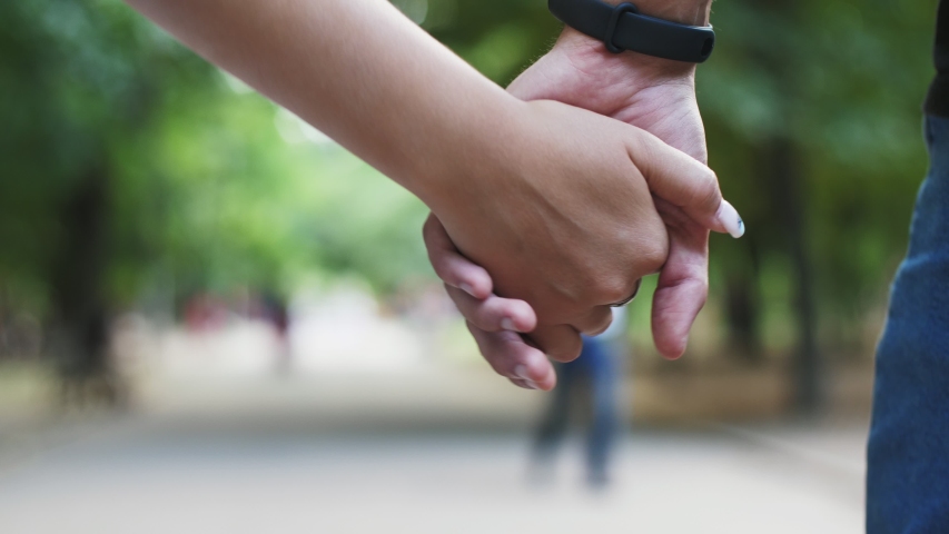  Romantic closeup of a young man`s hand with a wristwatch holding a young woman`s hand when the happy couple is moving in a green park in summer in slow motion. Royalty-Free Stock Footage #1036710839