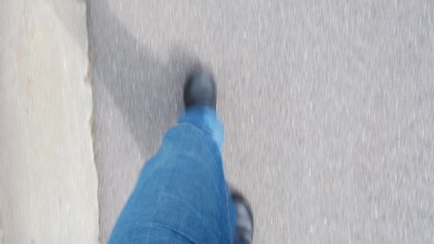Male feet in blue jeans walking on asphalt street