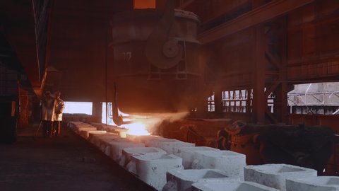 Iron foundry. Two steelworkers in protective clothing cast steel into molds.