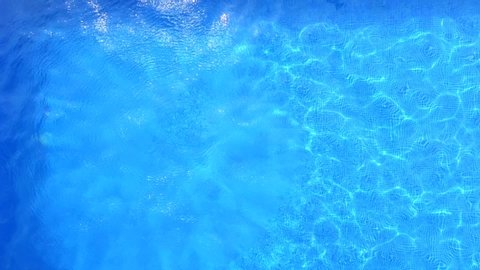 Aerial view of a young woman on summer vacation jumping head first into clear blue pool water in a sunny day. 