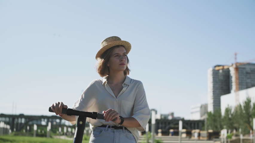 Young woman in straw hat walking with her the electric kick scooter