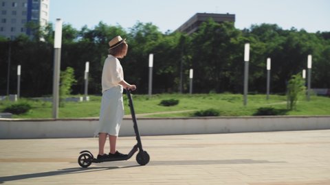 SIDE VIEW Attractive woman riding an electric city shared scooter in the city park