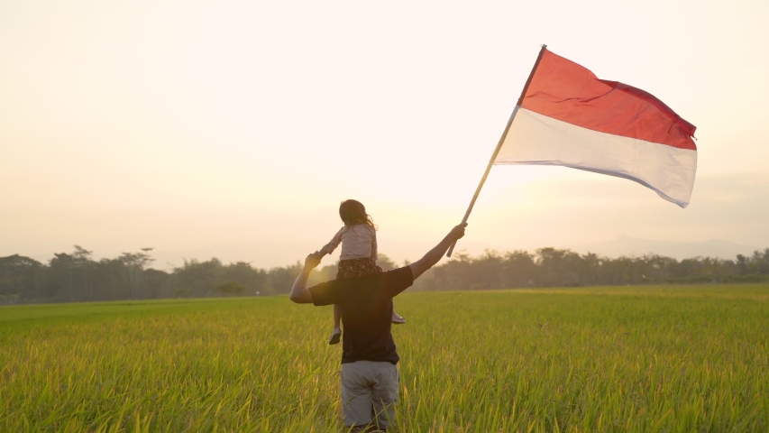 father carrying little girl pride flapping Indonesian flag with happiness in the rice field Royalty-Free Stock Footage #1036731932