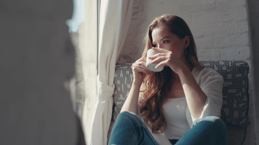 Gorgeous young woman in the house holding and drinking a cup of tea near the window smiling looking outside feel happy Royalty-Free Stock Footage #1036735622