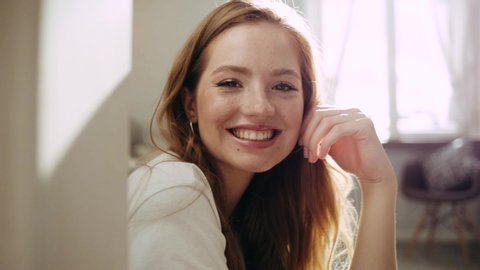 Cheerful gorgeous young european woman sitting at home looking away and at camera smiling and enjoying the moment