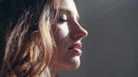 Close-up portrait of attractive young woman with cute freckles looking at sun in the apartment feel happy the sun is shining slow motion