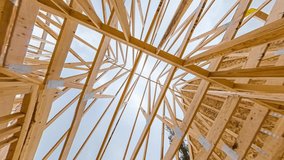 4k time lapse clip of wood roof beams of a new home construction site under blue sky and clouds passing by