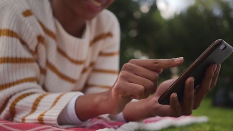 Close-up of an african young woman lying in the park using social media app on mobile phone