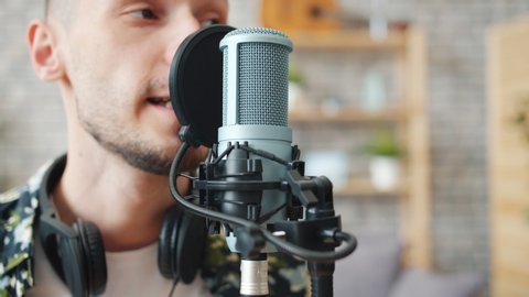 Slow motion of happy young bearded man talking in microphone recording podcast in studio smiling enjoying work. Audio blogging and modern people concept.