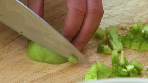 Handheld, close up shot of a green tomato being sliced by a large knife.