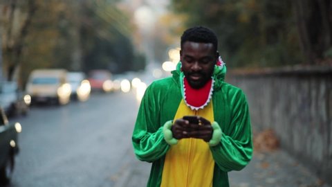 Happy dino young african man actor walking in the street using modern smartphone enjoying leisure time outdoors.