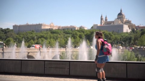 A cyclist man and a skater girl pass in front of the Almudena Cathedral and the Royal Palace of Madrid