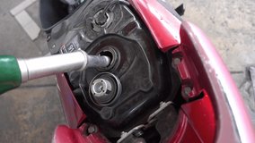 man holding fuel pump to tank of motorcycle in gas station.  