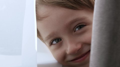 A cute little boy is hiding behind a curtain, looking out and having fun. Happy child playing hide and seek in the room.