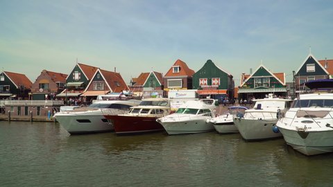 Volendam, North Holland / Netherlands - June 23rd, 2019: Leaving the Volendam harbor from a ferry / Colorful wooden houses in the waterfront / Moored boats in the harbor