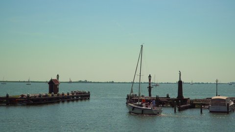 Volendam, North Holland / Netherlands - June 23rd, 2019: A sailboat leaving the Volendam harbor among two docks
