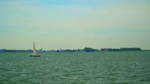 Volendam, North Holland / Netherlands - June 23rd, 2019: A sailboat between Marken and Volendam with the Monnickendam skyline in the distance
