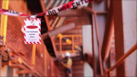 4 K footage of red and white danger tag  exclusion zone tape warning sign barricading working area as dropped object zone preventing from public access defocused worker background construction site 