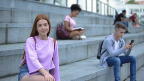 Beautiful red-haired teenager sitting stairs smiling camera, student exchange
