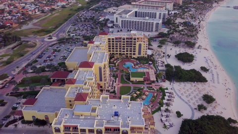 A massive yellow hotel with a pool on the beach of Aruba. Aerial sweep.
