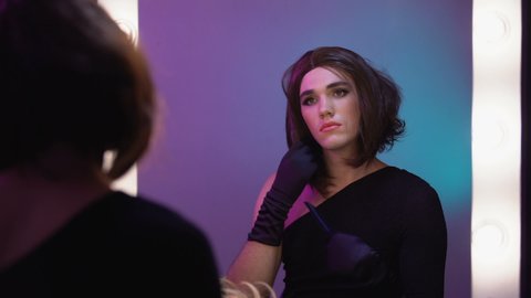 Non-binary person trying on wigs looking in mirror, choosing hairstyle for party