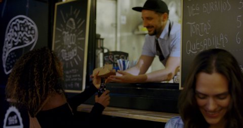 HANDHELD Cheerful waiter taking serving food to customers at counter, Mexican street food truck. 4K UHD RAW graded footage