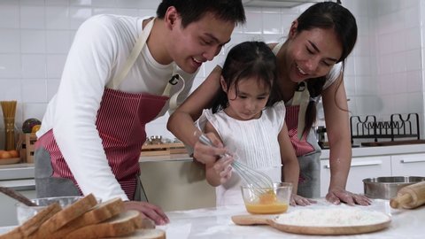 Happy Asian family Father, Mother and Daughter are beat eggs in bowl preparing the cookies in the kitchen. family cooking food Concept.
