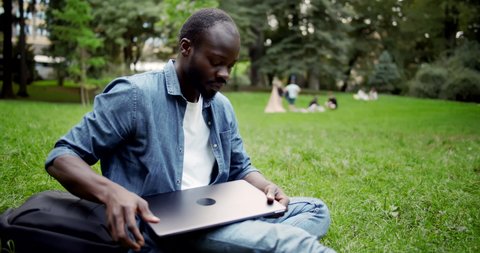 Afro-american male student opening laptop and starting to work, preparing educational project