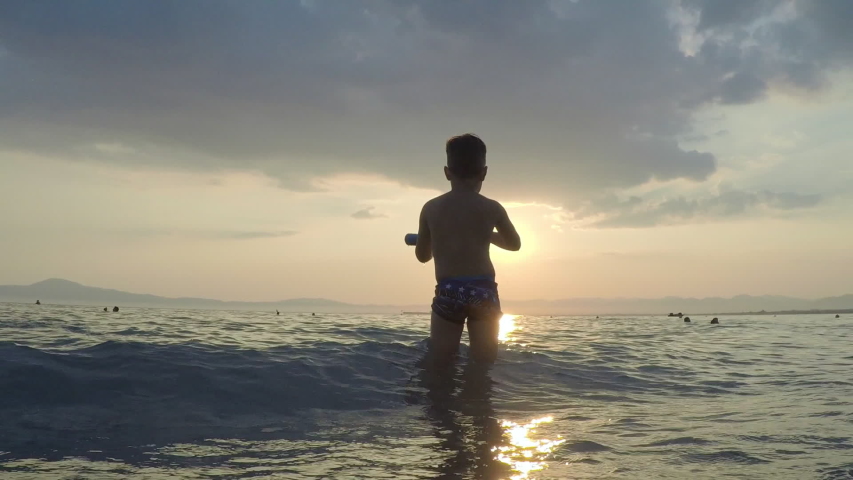 Kid plays at the waves with sunset on the background at Kalamata beach, Greece