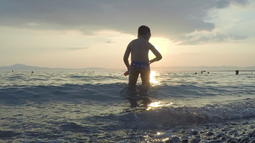 Kid plays at the waves with sunset on the background at Kalamata beach, Greece