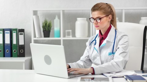 Focused young beautiful female doctor working using laptop pc at modern clinic